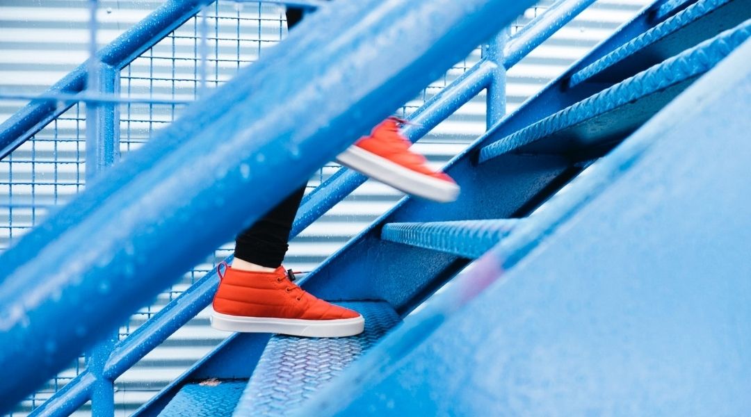 Human Resources 2022 neu gedacht: Mitarbeiter steigt in roten Sneakers eine blaue Treppe hoch.